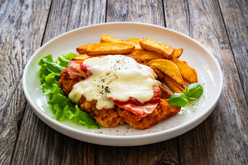 Milanesa Napolitana - fried breaded cutlet with ham, mozzarella cheese and tomato sauce on wooden background