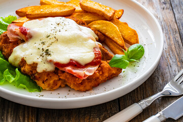 Milanesa Napolitana - fried breaded cutlet with ham, mozzarella cheese and tomato sauce on wooden background