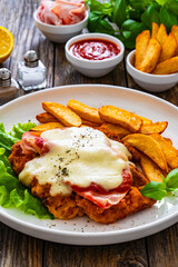 Milanesa Napolitana - fried breaded cutlet with ham, mozzarella cheese and tomato sauce on wooden background