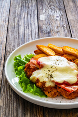 Milanesa Napolitana - fried breaded cutlet with ham, mozzarella cheese and tomato sauce on wooden background