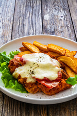 Milanesa Napolitana - fried breaded cutlet with ham, mozzarella cheese and tomato sauce on wooden background