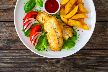 Seared cod loin with fried potatoes and fresh vegetables on wooden table