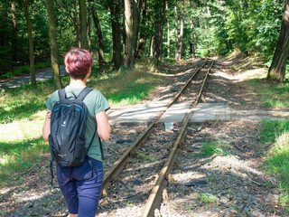 Attractive red hair girl backpacker walks on rails of narrow gauge Gablenz Kromlau, Germany