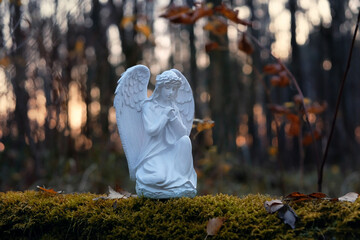 Praying angel figurine in autumn forest, dark natural abstract background. symbol of faith in God,...