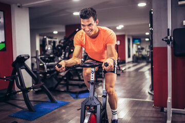 Fototapeta na wymiar Man biking in the gym, exercising legs doing cardio workout cycling bikes.