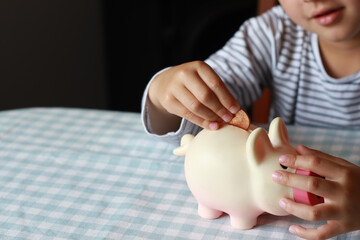 Obraz na płótnie Canvas Chid holding piggy bank. Child boy putting insert coins in the piggy bank for saving money. 