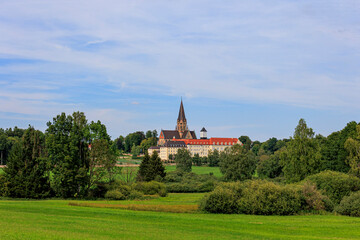 The church tower of St. Ottilien Monastery in Bavaria between forests and meadows under white blue...