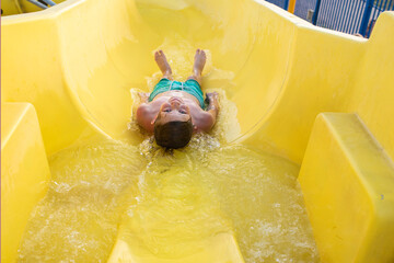  happy child slides down the yellow water slide in the water park. a joyful 10 year old boy has fun...