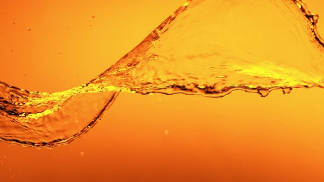 Super Slow Motion of Splashing Rotating Golden Liquid Isolated on Orange Background. Filmed on High Speed Cinema Camera, 1000 fps.