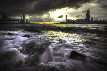hong kong city skyline at sunset with sea wave in foreground
