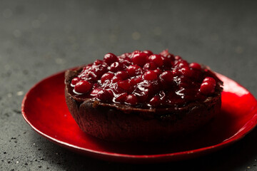 Delicious chocolate dessert with lingonberry jam on a glass red plate on a dark background,