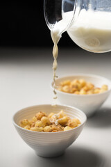 Breakfast cereal with granola and milk in small bowls with a glass decanter on a white background