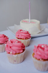 Cupcakes with pink whipped cream close-up on a white background. Holiday birthday. Bento cake with candles in the background