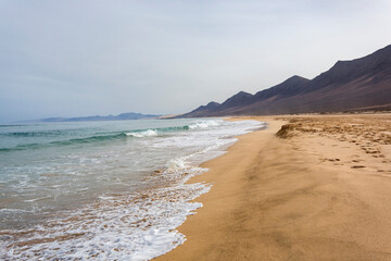 Playa paradisiaca en Fuerteventura en las Islas Canarias con las olas rompiendo en una arena fina y dorada bajo un cielo azul sin nubes