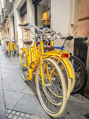 Group of yellow bikes for rent outside a bicycle rental shop on a European street.
