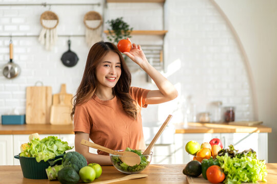 Portrait of beauty  healthy asian woman hold tomato, eating vegan food healthy with fresh vegetable salad in kitchen at home.diet, vegetarian, fruit, wellness, health, green food.Fitness, healthy food
