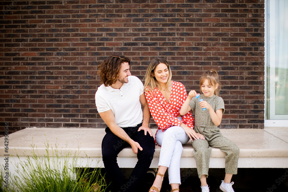 Wall mural Family with a mother, father and daughter sitting outside on the steps of a front porch of a brick house