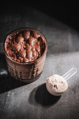Glass of healthy chocolate milkshake smoothie with protein powder on dark background