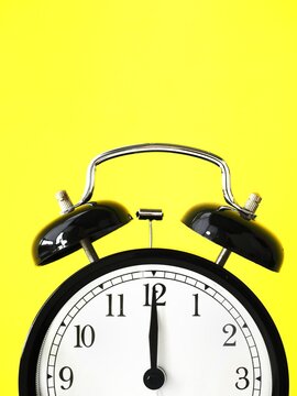 Black retro alarm clock at 12 twelve o clock on a yellow background with copy space to add text 12am 12pm