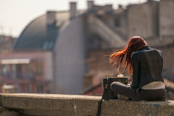 the wind swaying the red hair of a woman bathed in the rays of the midday sun on the roof of a...