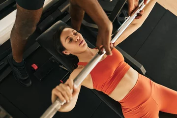 Gordijnen Black male trainer helping sportswoman with bench press exercise © kegfire