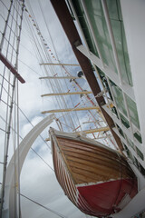 The bow of a wooden lifeboat against the background of the masts of a sailing ship