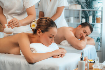 Obraz na płótnie Canvas Hot herbal ball spa massage body treatment, masseur gently compresses herb bag on couple customer body. Tranquil and serenity of aromatherapy recreation in day lighting ambient at spa salon. Quiescent