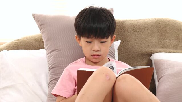 Asian handsome boy reading favorite book while lying down on bed at home, happy little kid spend time free to their advantage. Son enjoying  reading manga new story. staying at home in self isolation.