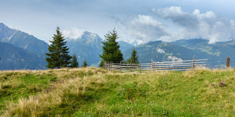 Panoramabild einer Bergwiese mit Holzzaun und im Hintergrund wolkenverhangene Berge