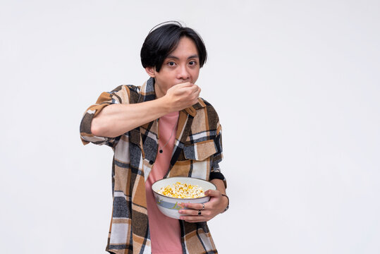 A young asian man gorging on popcorn while watching a movie. Isolated on a white background.