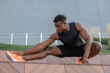 Naklejka premium Confident young African man in sportswear doing stretching exercises while training outdoors