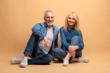 Happy senior man and woman sitting on floor, beige background