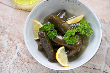 Greek dolmades served with fresh parsley and lemon wedges in a grey bowl, horizontal shot on a pinkish granite background, elevated view