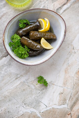Bowl with greek dolma or dolmades or vine leaves with stuffing, vertical shot on a beige granite background, copy space, above view
