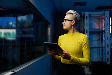 Female IT specialist standing with tablet looking through glass of server room