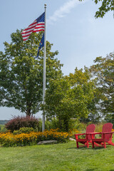 Flag pole with American flag flying and 2 red deck chairs in outdoor setting. 