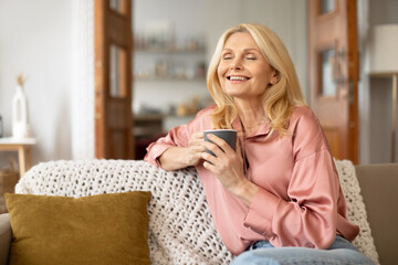 Joyful senior woman holding cup enjoying her morning coffee indoors