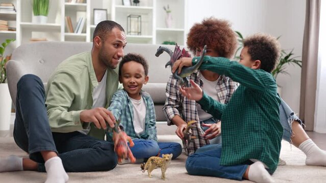 Lovely african american family of four playing together on floor of cozy apartment. Caring mother and father using animal figurines to developing charming imagination of two sons