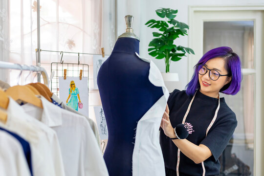 Fashionable freelance dressmaker is pinning her marking muslin for new dress by pinning to mannequin while working in her artistic workshop studio for fashion design and clothing business industry