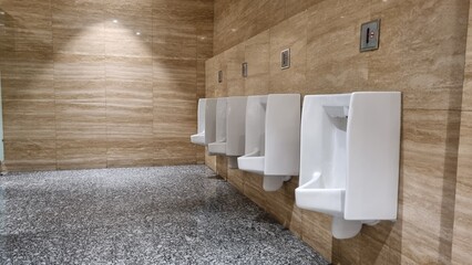 White urinals in men's bathroom. Men's restroom with white porcelain urinals in line. Modern clean public toilets with tiles. Comfort male toilet urinal concept.