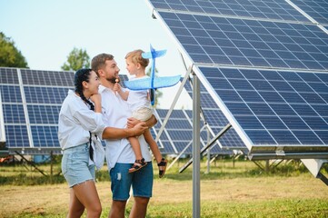 Young family of three is crouching near photovoltaic solar panel, little boy and parents. modern family concept. The concept of green energy