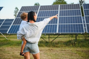 Happy mother and her little son are walking near the solar panels. The concept of green energy.