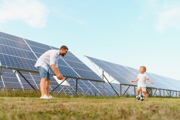 A father and his little son play soccer near the solar panels. The concept of renewable energy.