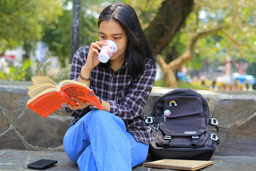 focused young asian woman reading a book with a cup of coffe in her hand