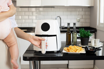 Woman cooking with modern Air fryer. Young mother with a baby in her hands. Lifestyle of new normal...
