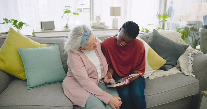 Assisted living, funny photo album and senior with a black woman caregiver on a sofa in the living room. Smile, laughing and elderly resident looking at a memory with a volunteer in a retirement home