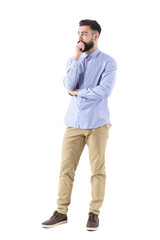 Young bearded adult business man in formalwear thinking and looking up with hand on chin. Full body length portrait isolated on transparent background.