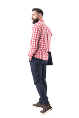 Back view of confident handsome young bearded man holding laptop and walking away. Full body isolated on transparent background.