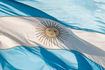 Full frame closeup photo of the Argentine flag, blue and white, with the yellow sun in the center, waving