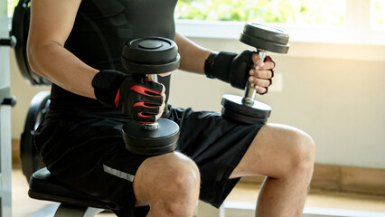 Athlete man in black sportswear wearing sport gloves sitting on workout bench at weightlifting station holding dumbbells prepare for lifting in fitness gym. Weight training and bodybuilding concepts